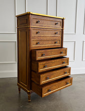 Load image into Gallery viewer, This stately Louis XVI–style chest combines generous storage with a tall, space-conscious silhouette. Crafted from mahogany solids with richly figured cerejeira veneers, it features seven spacious drawers framed by hand-applied gold accents. Fluted corner columns, paneled sides, decorative metal knobs, and tapered legs. Good Bones Furniture
