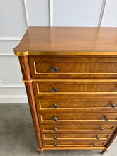 Load image into Gallery viewer, This stately Louis XVI–style chest combines generous storage with a tall, space-conscious silhouette. Crafted from mahogany solids with richly figured cerejeira veneers, it features seven spacious drawers framed by hand-applied gold accents. Fluted corner columns, paneled sides, decorative metal knobs, and tapered legs. Good Bones Furniture
