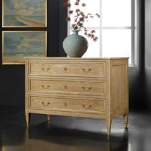 Load image into Gallery viewer, Introduce a touch of European-inspired elegance to your home with the Modern History French 3 Drawer Commode. Its gracefully contoured silhouette and gently tapered legs pay homage to classic French design. Crafted with an oak random veneer case, each piece highlights the natural, one-of-a-kind patterns and grain variations inherent in fine wood, ensuring a distinctive character that sets it apart. The commode’s antique brass accents and hardware provide a refined contrast, lending warmth and timeless appea
