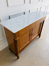 Load image into Gallery viewer, The Philippe Sideboard brings French Empire-inspired elegance and storage to a dining room, entryway, or living space. Crafted with richly figured cerejeira veneer, it features bookmatched door and drawer fronts, fluted columns, and hand-applied gold highlights. A polished white marble top creates a striking contrast with the warm wood tones. Two spacious drawers and a double-door cabinet with an interior shelf provide ample storage for serving pieces, linens, and other essentials. Good Bones Furniture
