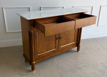 Load image into Gallery viewer, The Philippe Sideboard brings French Empire-inspired elegance and storage to a dining room, entryway, or living space. Crafted with richly figured cerejeira veneer, it features bookmatched door and drawer fronts, fluted columns, and hand-applied gold highlights. A polished white marble top creates a striking contrast with the warm wood tones. Two spacious drawers and a double-door cabinet with an interior shelf provide ample storage for serving pieces, linens, and other essentials. Good Bones Furniture
