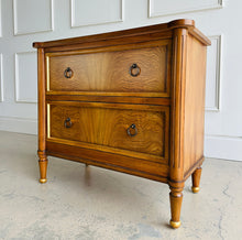 Load image into Gallery viewer, Elevate your bedside with the Riley Nightstand, a refined two-drawer piece that pairs timeless form with modern function. The front is clad in striking cerejeira veneer arranged in a radiant pattern and framed with hand-applied gold trim, while tapered legs finish with gilded caps for a subtle luxe note. Thoughtful scaling, warm mahogany tones, and elegant antique brass ring pulls make Riley an easy fit for both classic and contemporary bedrooms. Good Bones Furniture
