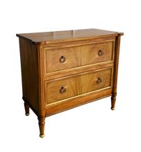 Load image into Gallery viewer, Elevate your bedside with the Riley Nightstand, a refined two-drawer piece that pairs timeless form with modern function. The front is clad in striking cerejeira veneer arranged in a radiant pattern and framed with hand-applied gold trim, while tapered legs finish with gilded caps for a subtle luxe note. Thoughtful scaling, warm mahogany tones, and elegant antique brass ring pulls make Riley an easy fit for both classic and contemporary bedrooms. Good Bones Furniture

