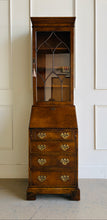 Load image into Gallery viewer, Classic English craftsmanship never goes out of style. This Southampton George III Style Secretary Bookcase is a beautifully proportioned piece that combines elegant display storage, a functional writing desk, and generous drawer storage within a refined, space-saving silhouette. Rich walnut and burl walnut veneers showcase striking natural grain throughout, while the leaded glass door, dentil crown molding, and original Chippendale-style brass hardware add timeless architectural character. Good Bones 

