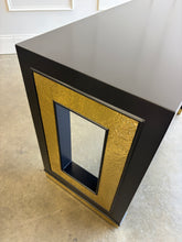 Load image into Gallery viewer, The Ashleigh Console by Theodore Alexander pairs a streamlined silhouette with dramatic decorative details. Professionally lacquered in black, it features substantial rectangular supports accented by textured gold panels, inset antiqued mirror, and brass-capped feet. Two discreet drawers provide concealed storage. Good Bones Furniture
