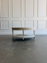 Load image into Gallery viewer, The Lucienne Cocktail Table by Theodore Alexander combines classical ornament with a light, graceful silhouette. Crafted from Khaya wood and richly figured Khaya swirl veneer, its round top rests above a fluted frieze accented with carved leaf motifs. Slender fluted legs connect the upper surface to a wide circular lower shelf.  Washed Blanchette finish. Good Bones Furniture
