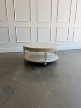 Load image into Gallery viewer, The Lucienne Cocktail Table by Theodore Alexander combines classical ornament with a light, graceful silhouette. Crafted from Khaya wood and richly figured Khaya swirl veneer, its round top rests above a fluted frieze accented with carved leaf motifs. Slender fluted legs connect the upper surface to a wide circular lower shelf.  Washed Blanchette finish. Good Bones Furniture
