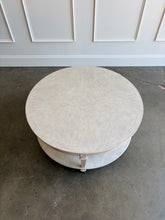 Load image into Gallery viewer, The Lucienne Cocktail Table by Theodore Alexander combines classical ornament with a light, graceful silhouette. Crafted from Khaya wood and richly figured Khaya swirl veneer, its round top rests above a fluted frieze accented with carved leaf motifs. Slender fluted legs connect the upper surface to a wide circular lower shelf.  Washed Blanchette finish. Good Bones Furniture
