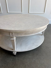 Load image into Gallery viewer, The Lucienne Cocktail Table by Theodore Alexander combines classical ornament with a light, graceful silhouette. Crafted from Khaya wood and richly figured Khaya swirl veneer, its round top rests above a fluted frieze accented with carved leaf motifs. Slender fluted legs connect the upper surface to a wide circular lower shelf.  Washed Blanchette finish. Good Bones Furniture
