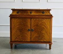Load image into Gallery viewer, The Valencia Bedside Chest combines elegant architectural detailing with beautifully figured wood grain. Crafted from mahogany solids with richly patterned cerejeira veneers, it features two cabinet doors that open to reveal a spacious interior with one adjustable shelf. molded top, graceful concave frieze, decorative metal hardware, and fluted tapered feet. Good Bones Furniture
