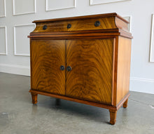 Load image into Gallery viewer, The Valencia Bedside Chest combines elegant architectural detailing with beautifully figured wood grain. Crafted from mahogany solids with richly patterned cerejeira veneers, it features two cabinet doors that open to reveal a spacious interior with one adjustable shelf. molded top, graceful concave frieze, decorative metal hardware, and fluted tapered feet. Good Bones Furniture

