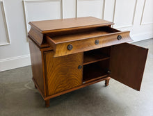 Load image into Gallery viewer, The Valencia Bedside Chest combines elegant architectural detailing with beautifully figured wood grain. Crafted from mahogany solids with richly patterned cerejeira veneers, it features two cabinet doors that open to reveal a spacious interior with one adjustable shelf. molded top, graceful concave frieze, decorative metal hardware, and fluted tapered feet. Good Bones Furniture
