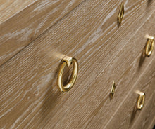 Load image into Gallery viewer, The Ventura Dresser by Modern History offers a refined balance of texture, craftsmanship, and understated luxury. Wrapped in oak random veneer, the surface highlights the natural variation of the wood grain, creating subtle depth and visual movement across the broad drawer fronts. The warm oak tone pairs beautifully with polished solid brass ring pulls and matching escutcheons, lending the piece a timeless, tailored character. Good Bones Furniture
