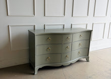 Load image into Gallery viewer, This vintage Table Rock dresser pairs classic construction with a fresh, tailored finish. Lacquered in Sherwin Williams Lauriston Stone, the muted green-gray tone gives the piece a soft, updated presence while still feeling timeless. The gently serpentine front adds movement and elegance, and the new solid brass ring hardware brings a polished contrast to the clean drawer layout. Good Bones Furniture
