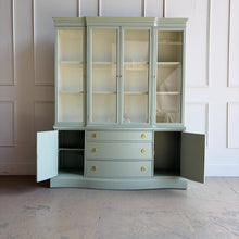Load image into Gallery viewer, This vintage Bassett China Cabinet has been professionally lacquered in Benjamin Moore Saybrook Sage on the exterior with a creamy white interior for a bright, clean display. The classic silhouette features four glass doors on the upper hutch for showcasing china, glassware, and collections, while the lower cabinet offers a graceful serpentine front with ample closed storage. Warm brass knobs finish the look with an elegant, timeless contrast. Good Bones Furniture
