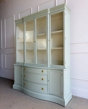 Load image into Gallery viewer, This vintage Bassett China Cabinet has been professionally lacquered in Benjamin Moore Saybrook Sage on the exterior with a creamy white interior for a bright, clean display. The classic silhouette features four glass doors on the upper hutch for showcasing china, glassware, and collections, while the lower cabinet offers a graceful serpentine front with ample closed storage. Warm brass knobs finish the look with an elegant, timeless contrast. Good Bones Furniture
