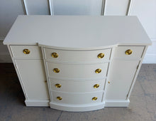 Load image into Gallery viewer, This vintage buffet combines generous storage with a compact, beautifully balanced silhouette. Professionally lacquered in a warm Custom Cream, it features a subtly bowed center with four spacious drawers, two smaller side drawers, and flanking cabinets with interior shelves. New brass Hepplewhite hardware. Good Bones Furniture
