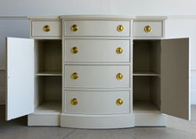 Load image into Gallery viewer, This vintage buffet combines generous storage with a compact, beautifully balanced silhouette. Professionally lacquered in a warm Custom Cream, it features a subtly bowed center with four spacious drawers, two smaller side drawers, and flanking cabinets with interior shelves. New brass Hepplewhite hardware. Good Bones Furniture
