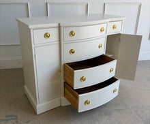 Load image into Gallery viewer, This vintage buffet combines generous storage with a compact, beautifully balanced silhouette. Professionally lacquered in a warm Custom Cream, it features a subtly bowed center with four spacious drawers, two smaller side drawers, and flanking cabinets with interior shelves. New brass Hepplewhite hardware. Good Bones Furniture
