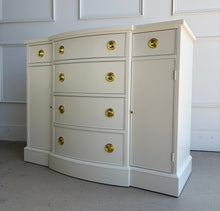 Load image into Gallery viewer, This vintage buffet combines generous storage with a compact, beautifully balanced silhouette. Professionally lacquered in a warm Custom Cream, it features a subtly bowed center with four spacious drawers, two smaller side drawers, and flanking cabinets with interior shelves. New brass Hepplewhite hardware. Good Bones Furniture
