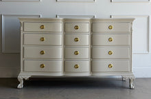 Load image into Gallery viewer, This vintage 12 drawer dresser by Continental Furniture has been professionally lacquered in Benjamin Moore Natural Linen, giving the traditional silhouette a softer, updated presence while highlighting its elegant serpentine front and carved details. Resting on sculpted claw feet with fluted corner accents, new Hepplewhite hardware. Good Bones Furniture
