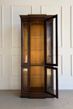 Load image into Gallery viewer, This vintage curio cabinet is a tall, architectural display piece designed to show off collections without overwhelming a room. A narrow footprint makes it an easy fit for dining rooms, living spaces, or entryways, while the glass-front design and interior light create a true “gallery” effect. Glass shelving and framed panels keep the silhouette light and refined, and the substantial crown and stepped base give it a classic, furniture-quality presence.
