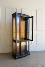 Load image into Gallery viewer, This vintage curio cabinet is a tall, architectural display piece designed to show off collections without overwhelming a room. A narrow footprint makes it an easy fit for dining rooms, living spaces, or entryways, while the glass-front design and interior light create a true “gallery” effect. Glass shelving and framed panels keep the silhouette light and refined, and the substantial crown and stepped base give it a classic, furniture-quality presence.

