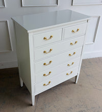 Load image into Gallery viewer, Vintage Dixie chest offers generous storage within a tall, space-conscious silhouette. Professionally lacquered in Benjamin Moore Swiss Coffee at 150% strength, its warm creamy-white finish complements the chest’s clean lines, inset drawer fronts, and tapered legs. Six drawers provide ample storage, while new solid brass drop-bail pulls add a polished contrast. Good Bones Furniture
