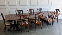 Load image into Gallery viewer, This vintage Drexel Heritage Nine Elms dining set showcases richly figured crotch mahogany veneer framed by contrasting banding. The expansive table rests on two ornately carved pedestal bases and includes three 22-inch leaves, extending it to an impressive 140 inches for large gatherings. Eight coordinating chairs—two armchairs and six side chairs. Good Bones Furniture
