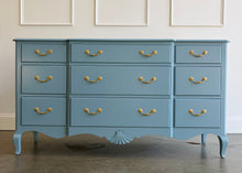 Load image into Gallery viewer, This vintage nine-drawer dresser by Ethan Allen combines generous storage with graceful traditional detailing. Professionally lacquered in a custom muted blue with soft gray undertones, the finish gives its classic silhouette a fresh, versatile look. Nine drawers provide abundant organized storage, while framed drawer fronts, a gently stepped top, curved apron, carved shell motif, and cabriole-style legs preserve its vintage character. Good Bones Furniture
