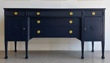 Load image into Gallery viewer, This vintage genuine mahogany sideboard combines generous storage with elegant Federal-inspired detailing. Professionally lacquered in Benjamin Moore In the Navy, its deep, classic navy finish highlights the fluted frieze, carved rosettes, decorative urn motifs, and slender tapered legs. New brass hardware. Good Bones Furniture
