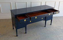 Load image into Gallery viewer, This vintage genuine mahogany sideboard combines generous storage with elegant Federal-inspired detailing. Professionally lacquered in Benjamin Moore In the Navy, its deep, classic navy finish highlights the fluted frieze, carved rosettes, decorative urn motifs, and slender tapered legs. New brass hardware. Good Bones Furniture
