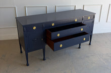 Load image into Gallery viewer, This vintage genuine mahogany sideboard combines generous storage with elegant Federal-inspired detailing. Professionally lacquered in Benjamin Moore In the Navy, its deep, classic navy finish highlights the fluted frieze, carved rosettes, decorative urn motifs, and slender tapered legs. New brass hardware. Good Bones Furniture
