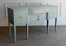 Load image into Gallery viewer, This vintage sideboard pairs a historic Hepplewhite-inspired silhouette with an unexpected modern color. Its gently bowed front, symmetrical layout, slender tapered legs, and balanced proportions reflect classic Federal design. Professionally lacquered in Sherwin-Williams Unusual Gray with new solid brass oval bail pulls with ornate neoclassical backplates. Good Bones Furniture
