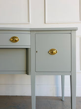 Load image into Gallery viewer, This vintage sideboard pairs a historic Hepplewhite-inspired silhouette with an unexpected modern color. Its gently bowed front, symmetrical layout, slender tapered legs, and balanced proportions reflect classic Federal design. Professionally lacquered in Sherwin-Williams Unusual Gray with new solid brass oval bail pulls with ornate neoclassical backplates. Good Bones Furniture

