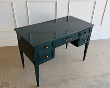 Load image into Gallery viewer, This beautifully refinished vintage desk offers timeless design with a fresh, designer-inspired finish. Professionally lacquered in Sherwin-Williams Rookwood Sash Green in a high-gloss sheen, it makes a bold yet sophisticated statement while preserving its classic mid-century silhouette. Five spacious drawers provide practical storage for office essentials, and the new antiqued brass hardware adds warmth and elegance against the rich green lacquer. Good Bones Furniture
