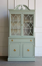 Load image into Gallery viewer, This vintage china cabinet blends classic form with a fresh, tailored finish. Professionally lacquered in Benjamin Moore Saybrook Sage on the exterior and paired with a creamy white interior, it offers a soft contrast that brightens the display space and gives the piece a custom, updated feel. Arched fretwork glass doors and a sculptural pediment. Good Bones Furniture
