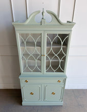 Load image into Gallery viewer, This vintage china cabinet blends classic form with a fresh, tailored finish. Professionally lacquered in Benjamin Moore Saybrook Sage on the exterior and paired with a creamy white interior, it offers a soft contrast that brightens the display space and gives the piece a custom, updated feel. Arched fretwork glass doors and a sculptural pediment. Good Bones Furniture
