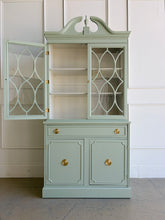 Load image into Gallery viewer, This vintage china cabinet blends classic form with a fresh, tailored finish. Professionally lacquered in Benjamin Moore Saybrook Sage on the exterior and paired with a creamy white interior, it offers a soft contrast that brightens the display space and gives the piece a custom, updated feel. Arched fretwork glass doors and a sculptural pediment. Good Bones Furniture
