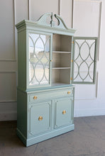 Load image into Gallery viewer, This vintage china cabinet blends classic form with a fresh, tailored finish. Professionally lacquered in Benjamin Moore Saybrook Sage on the exterior and paired with a creamy white interior, it offers a soft contrast that brightens the display space and gives the piece a custom, updated feel. Arched fretwork glass doors and a sculptural pediment. Good Bones Furniture
