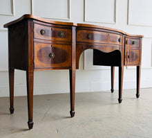 Load image into Gallery viewer, This vintage mahogany sideboard features graceful serpentine lines and exquisite satinwood inlay that highlight its timeless Federal-inspired design. The shaped top showcases a delicate inlaid urn motif, while bowed drawer fronts and paneled cabinet doors add depth and character throughout. A center drawer is flanked by two drawers above spacious side cabinets, providing generous storage for dining essentials or entertaining pieces. Good Bones Furniture
