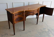 Load image into Gallery viewer, This vintage mahogany sideboard features graceful serpentine lines and exquisite satinwood inlay that highlight its timeless Federal-inspired design. The shaped top showcases a delicate inlaid urn motif, while bowed drawer fronts and paneled cabinet doors add depth and character throughout. A center drawer is flanked by two drawers above spacious side cabinets, providing generous storage for dining essentials or entertaining pieces. Good Bones Furniture
