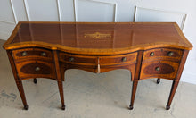 Load image into Gallery viewer, This vintage mahogany sideboard features graceful serpentine lines and exquisite satinwood inlay that highlight its timeless Federal-inspired design. The shaped top showcases a delicate inlaid urn motif, while bowed drawer fronts and paneled cabinet doors add depth and character throughout. A center drawer is flanked by two drawers above spacious side cabinets, providing generous storage for dining essentials or entertaining pieces. Good Bones Furniture
