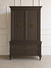 Load image into Gallery viewer, This vintage Mediterranean armoire has bold 1970s Spanish Revival styling with carved frieze detail, stepped door panels, burl veneer accents, and original brass ring hardware. The warm walnut-toned finish highlights the depth of the veneer, while the interior offers generous concealed storage with built-in drawers. Good Bones Furniture
