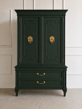 Load image into Gallery viewer, This vintage Mediterranean armoire has bold 1970s Spanish Revival styling with carved frieze detail, stepped door panels, burl veneer accents, and original brass ring hardware. The warm walnut-toned finish highlights the depth of the veneer, while the interior offers generous concealed storage with built-in drawers. Good Bones Furniture
