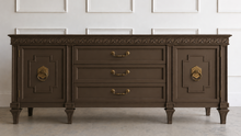 Load image into Gallery viewer, This vintage Mediterranean/ Spanish Revival credenza dresser has the scale, craftsmanship, and presence that make 1970s American case goods so collectible. The design features a carved scrolling frieze, burl veneer door panels, architectural legs, and original brass ring hardware with geometric backplates. Good Bones Furniture
