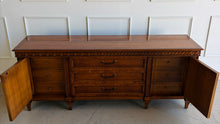 Load image into Gallery viewer, This vintage Mediterranean/ Spanish Revival credenza dresser has the scale, craftsmanship, and presence that make 1970s American case goods so collectible. The design features a carved scrolling frieze, burl veneer door panels, architectural legs, and original brass ring hardware with geometric backplates. Good Bones Furniture
