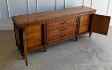 Load image into Gallery viewer, This vintage Mediterranean/ Spanish Revival credenza dresser has the scale, craftsmanship, and presence that make 1970s American case goods so collectible. The design features a carved scrolling frieze, burl veneer door panels, architectural legs, and original brass ring hardware with geometric backplates. Good Bones Furniture
