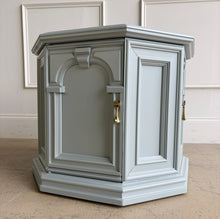 Load image into Gallery viewer, Professionally lacquered in Benjamin Moore Boothbay Gray, this vintage octagonal accent cabinet blends Hollywood Regency glamour with architectural neo-classical detailing. The octagonal silhouette, recessed panel molding, and arched faux-door styling give the piece strong boutique showroom presence. End table. Good Bones Furniture
