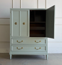 Load image into Gallery viewer, This vintage Thomasville armoire professionally lacquered in a custom muted green with soft blue-gray undertones, while the interior is finished in French Roast. Four paneled doors open to reveal divided upper compartments and two pull-out tray drawers. Two spacious lower drawers offer additional concealed storage. Good Bones Furniture
